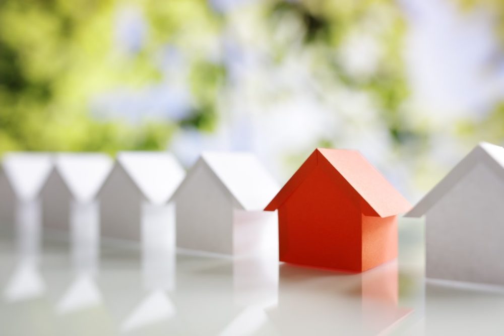 A line of white paper houses with a single red house standing out in the center, symbolising one of the questions to ask a real estate agent when selling is timing and market conditions.